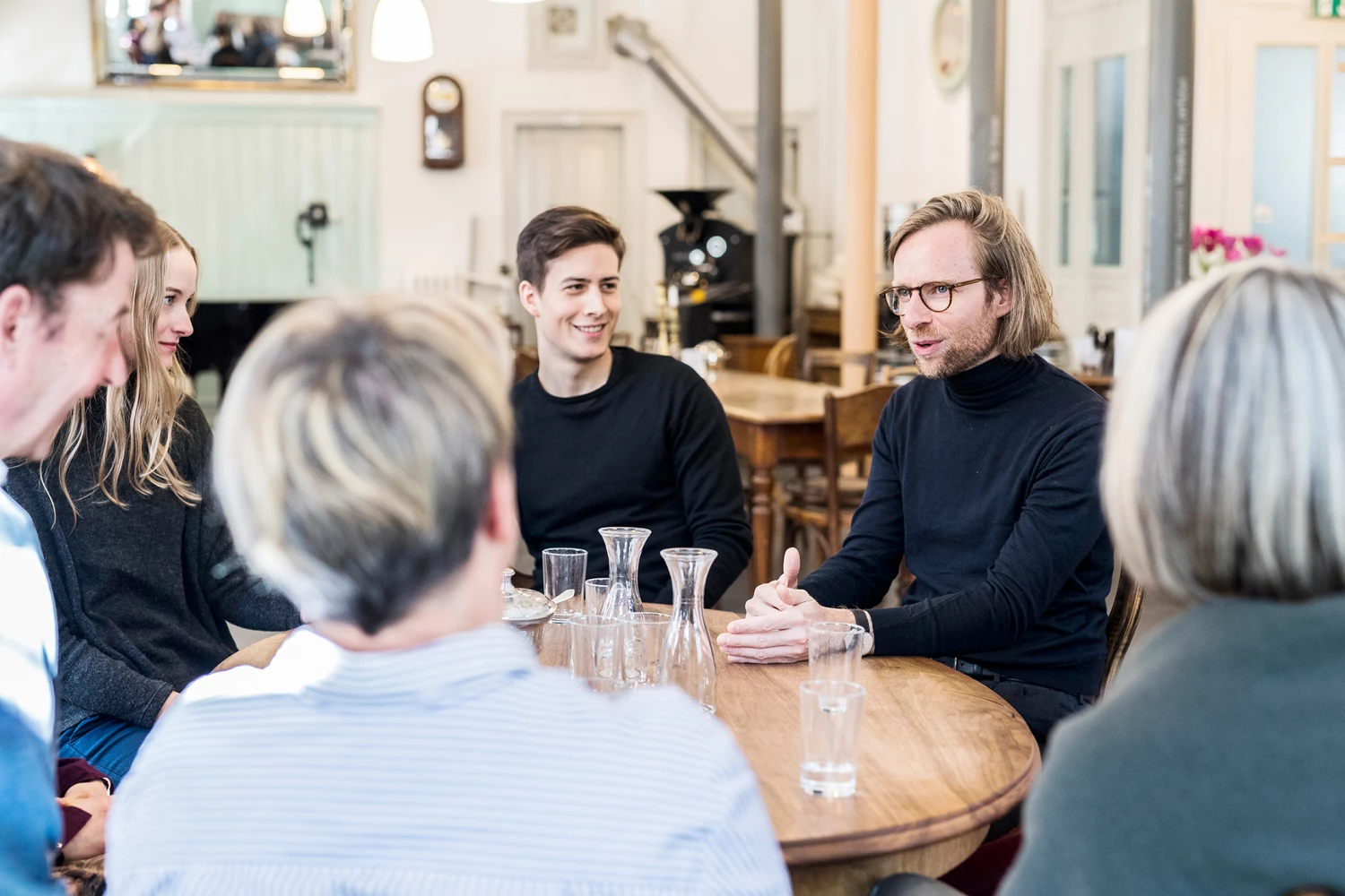 Eine Gruppe Menschen sitzt um einen runden Tisch und unterhält sich.