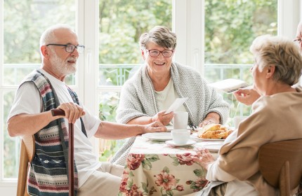 Drei Senior:innen sitzen an einem Tisch, trinken Kaffee und unterhalten sich.