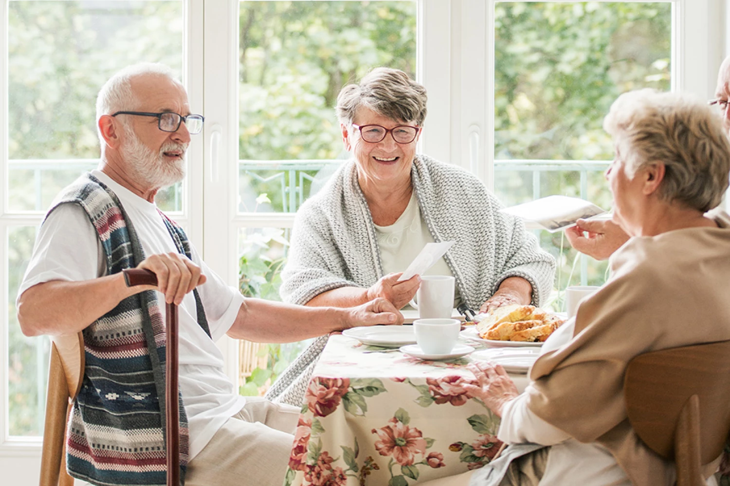 Drei Senior:innen sitzen an einem Tisch, trinken Kaffee und unterhalten sich.