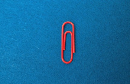 Eine rote B&uuml;roklammer auf blauem Filzuntergrund