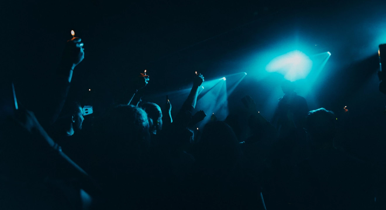 In einem abgedunkelten Saal halten etliche Konzertbesuchende brennende Feuerzeuge in die Höhe und lauschen der Musik.