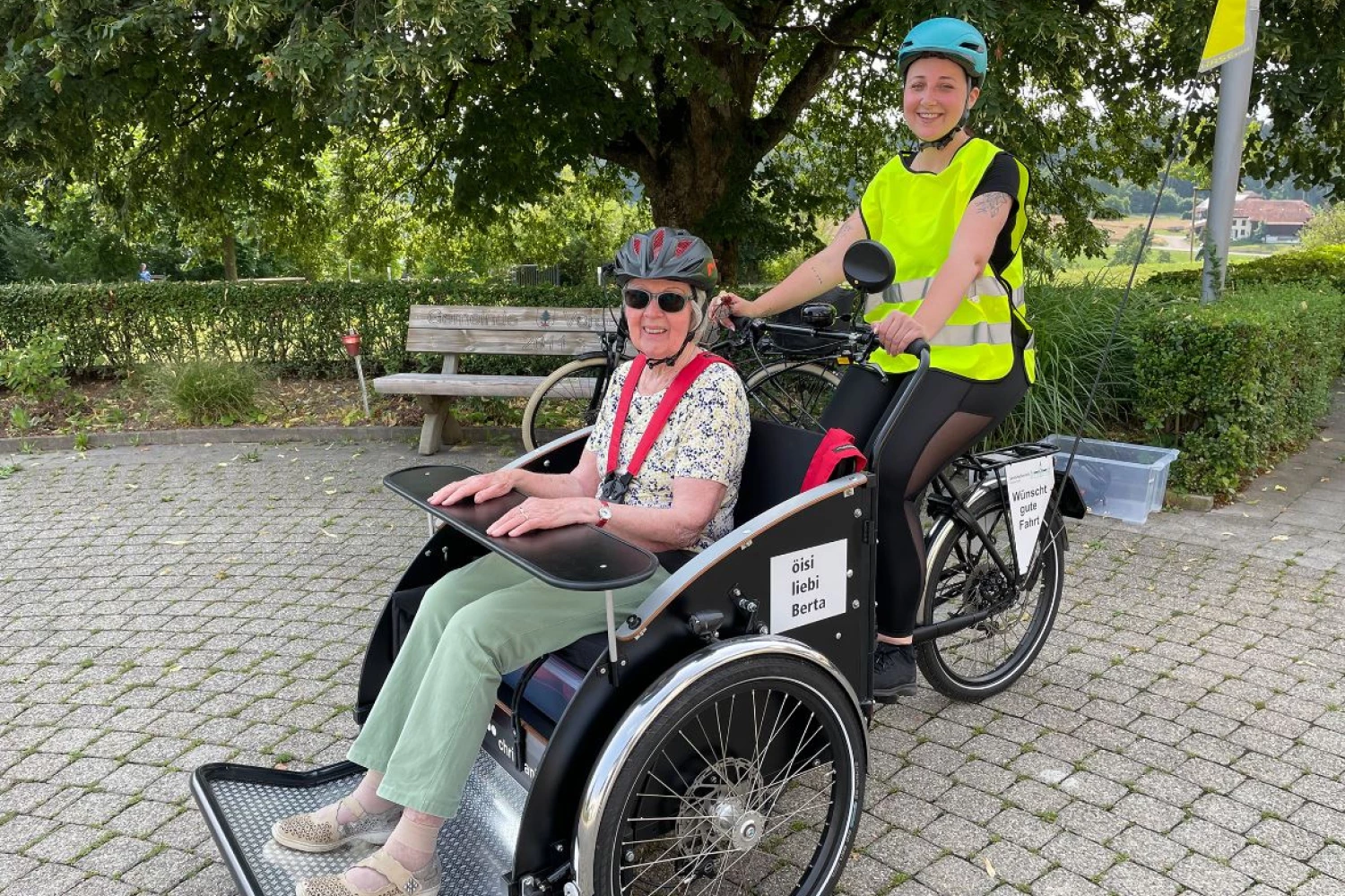 Das Bild zeigt eine Freiwillige auf einer E-Rikscha gemeinsam mit einer Bewohnerin eines Pflegeheims.