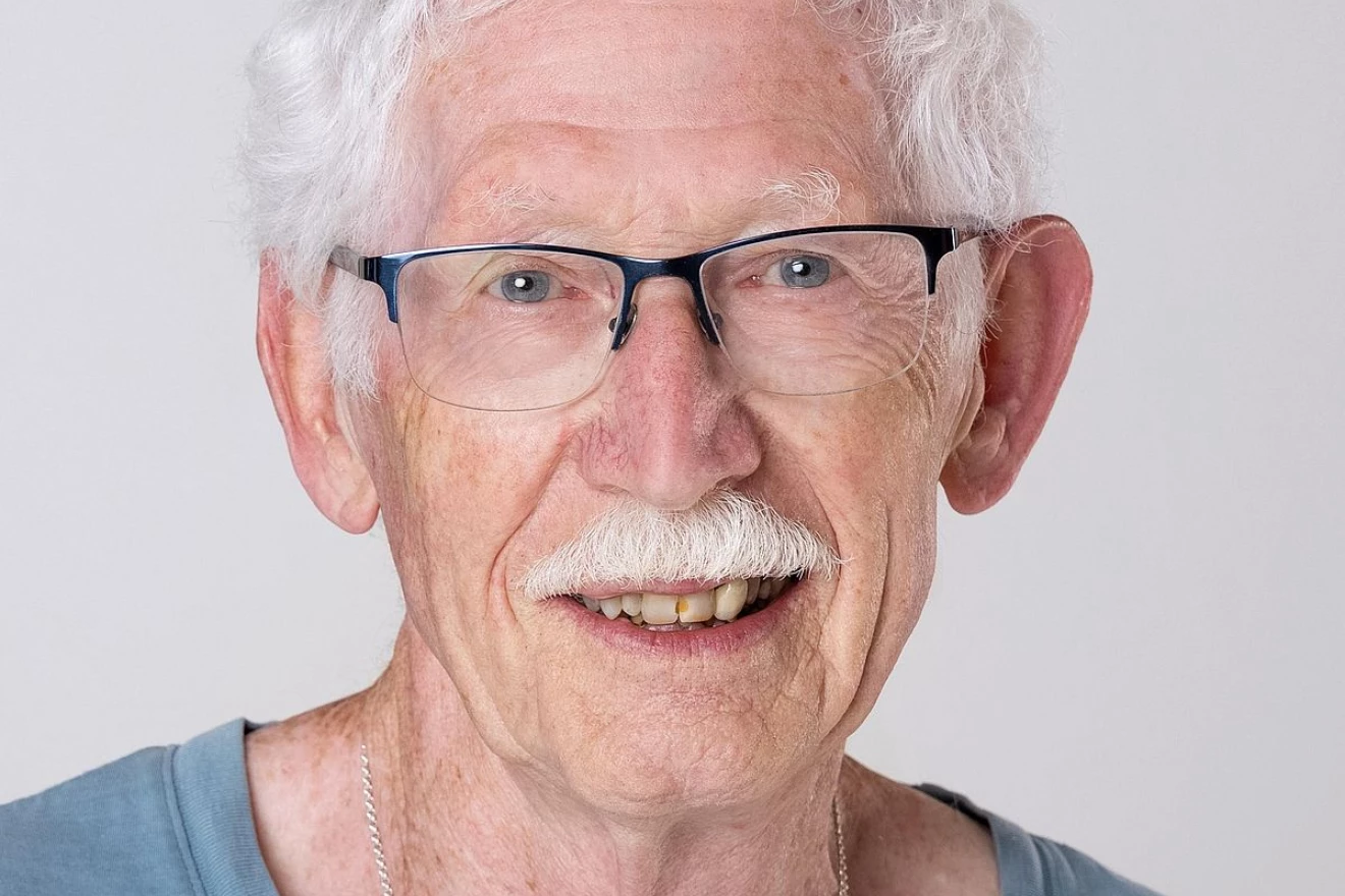 Beim Bild handelt es sich um ein Portrait-Foto eines älteren Freiwilligen, der freundlich in die Kamera lächelt.
