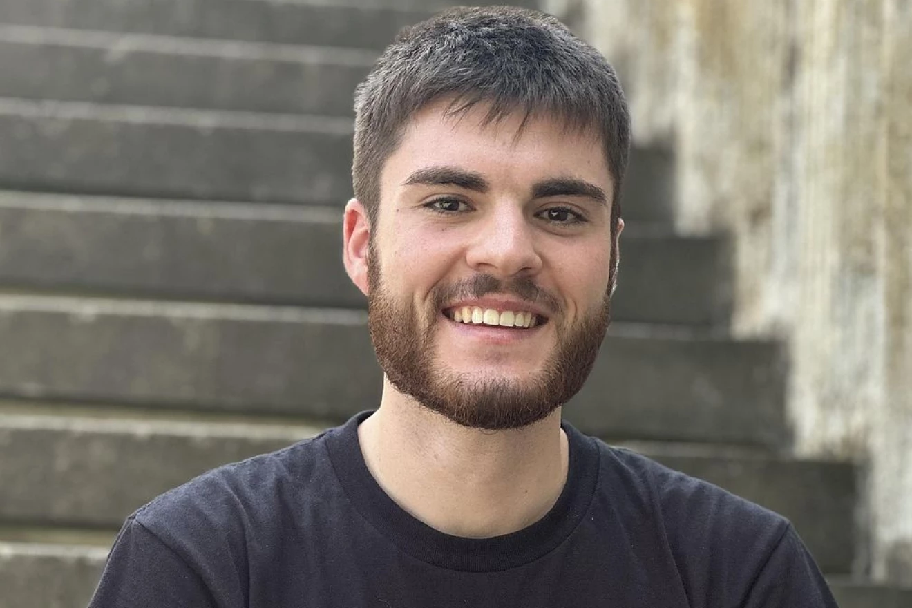 Portrait Foto eines jungen Freiwilligen, der im Freien auf einer Treppe sitzt und freundlich in die Kamera läüchelt.