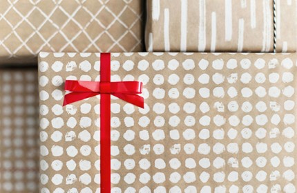 Das Bild zeigt vier in Packpapier verpackte Geschenke, wobei das Geschenk im Zentrum mit einer auffallend roten Schleife geschmückt ist.