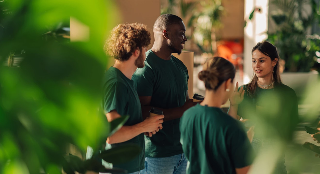 Eine stehende Gruppe von Freiwilligen in grünen T-Shirt mit Jeans bespricht sich.