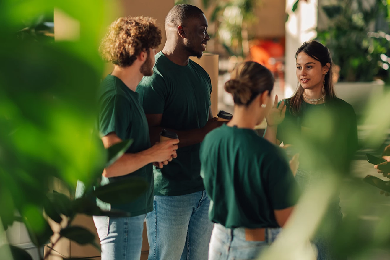Eine stehende Gruppe von Freiwilligen in grünen T-Shirt mit Jeans bespricht sich.