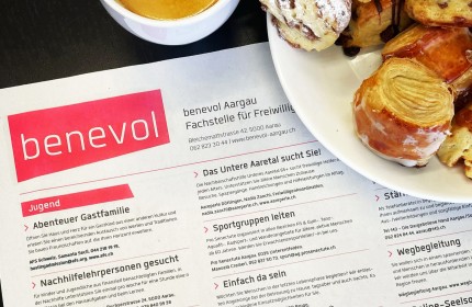 Zu sehen ist ein Foto des Freiwilligen-Stellenanzeigers von benevol Aargau in einer Zeitung sowie Teile eines Kaffees und einem Teller mit Kaffeegebäck.