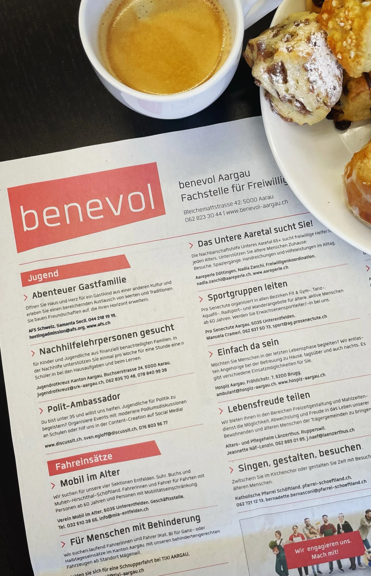 Zu sehen ist ein Foto des Freiwilligen-Stellenanzeigers von benevol Aargau in einer Zeitung sowie Teile eines Kaffees und einem Teller mit Kaffeegebäck.